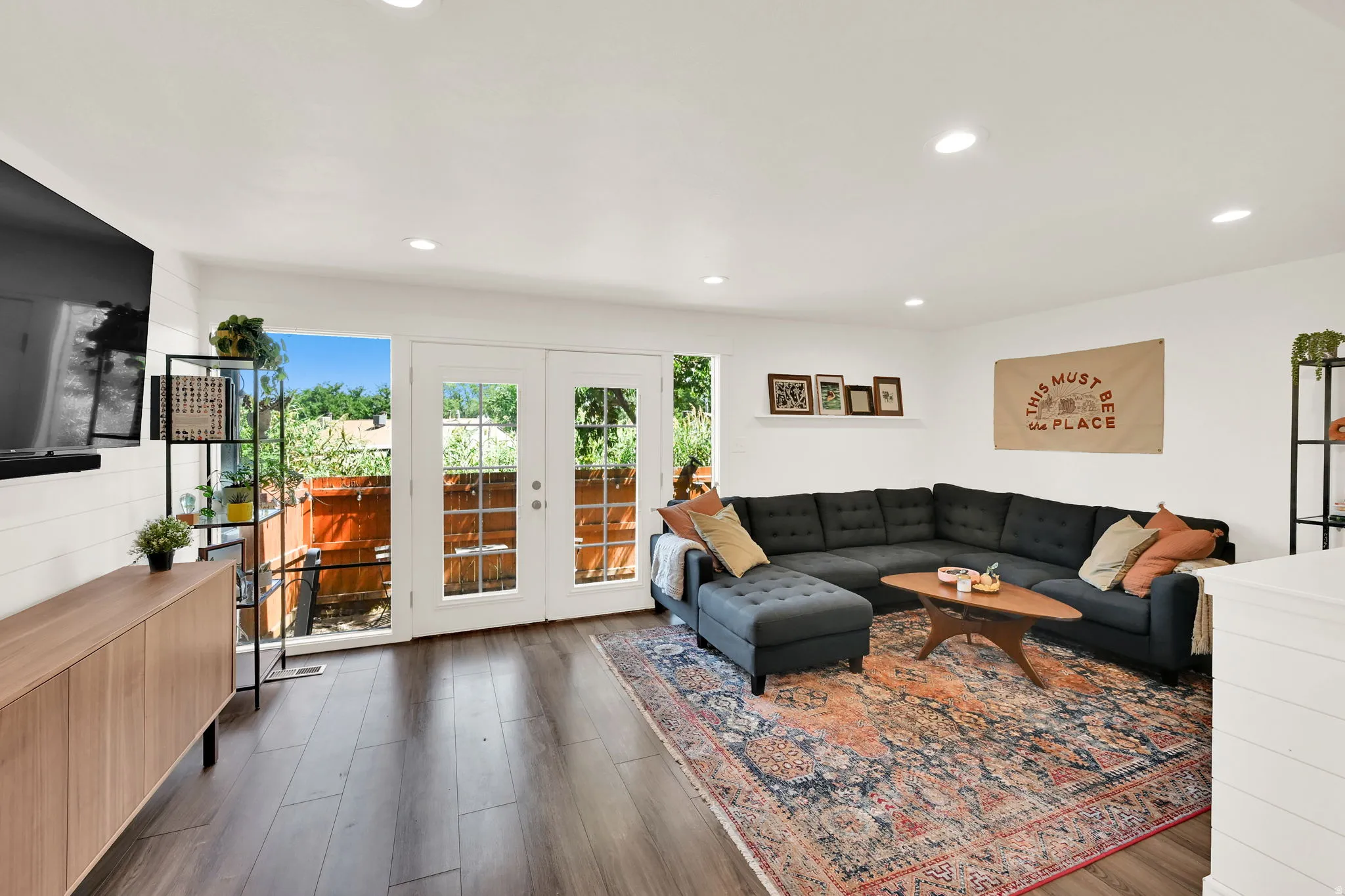 Recessed lighting illuminates the living area featuring wood-finish flooring and a white shiplap-style accent wall