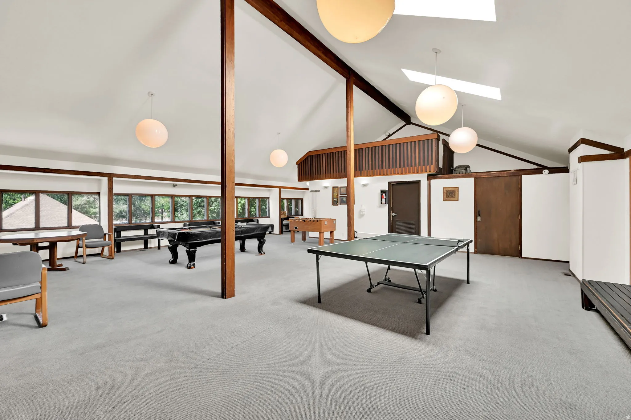 Vaulted ceilings with exposed beams, multiple skylights, perimeter windows, and a carpeted floor