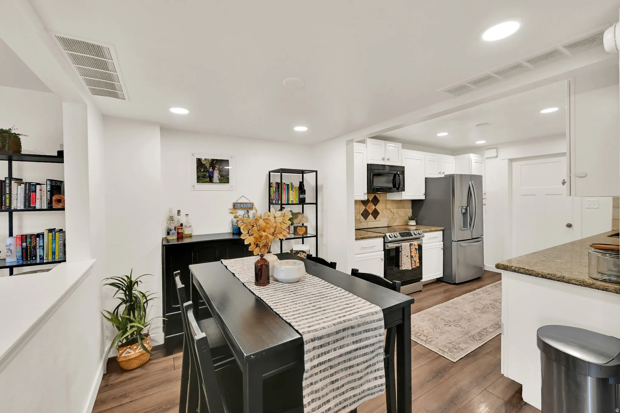 Open-concept kitchen and dining area featuring recessed lighting, wood-finish flooring, and white cabinetry