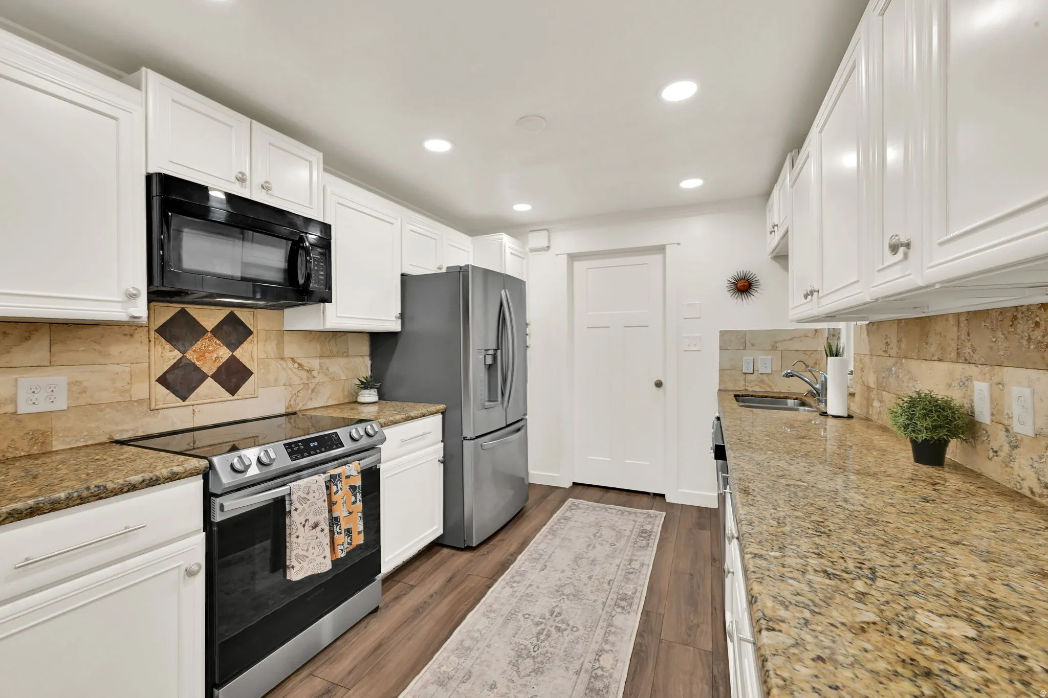 Granite countertops, white shaker cabinetry, stainless steel appliances, tile backsplash, and wood-finish flooring