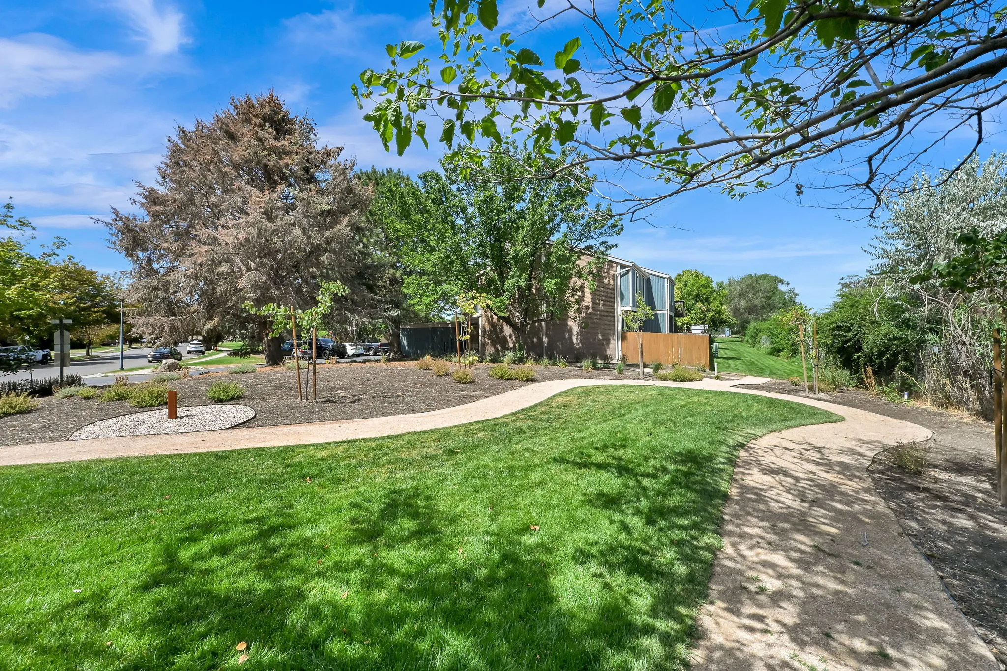 Expansive green space featuring a manicured lawn, winding gravel paths, mature trees, and a privacy fence bordering the property