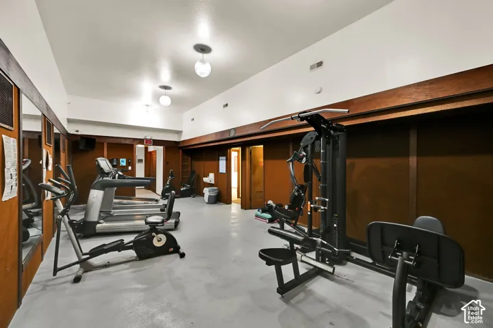 Spacious fitness area featuring wall-mounted mirrors, recessed lighting, and wood-paneled walls