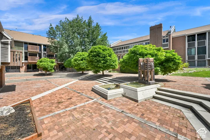 Expansive brick courtyard featuring mature trees, concrete steps, and a multi-tiered water feature with a central sculpture