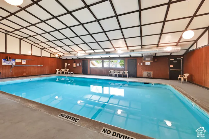 Indoor swimming pool with concrete decking, wood-paneled walls, and a vaulted grid ceiling with integrated lighting