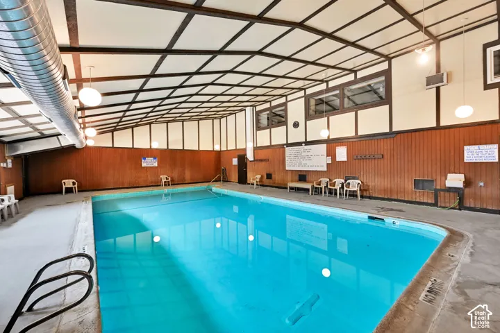 Indoor swimming pool with concrete decking, wood-paneled walls, and a beamed ceiling