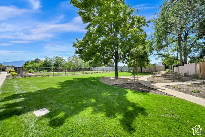 Expansive green lawn, mature trees, gravel pathways, perimeter fencing, and distant mountain backdrop