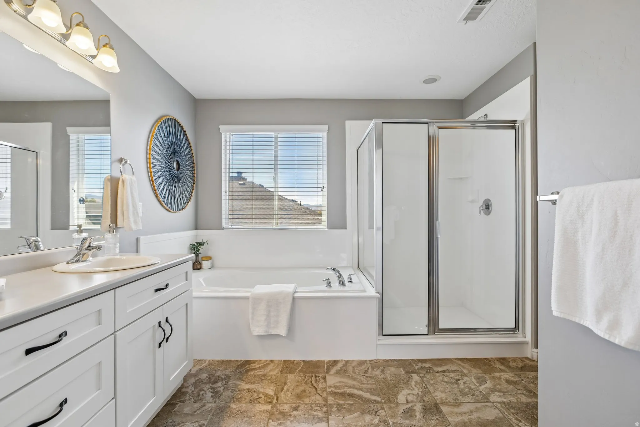 Bathroom featuring a built-in tub, separate shower with a glass enclosure, dual-sink vanity, and tiled flooring
