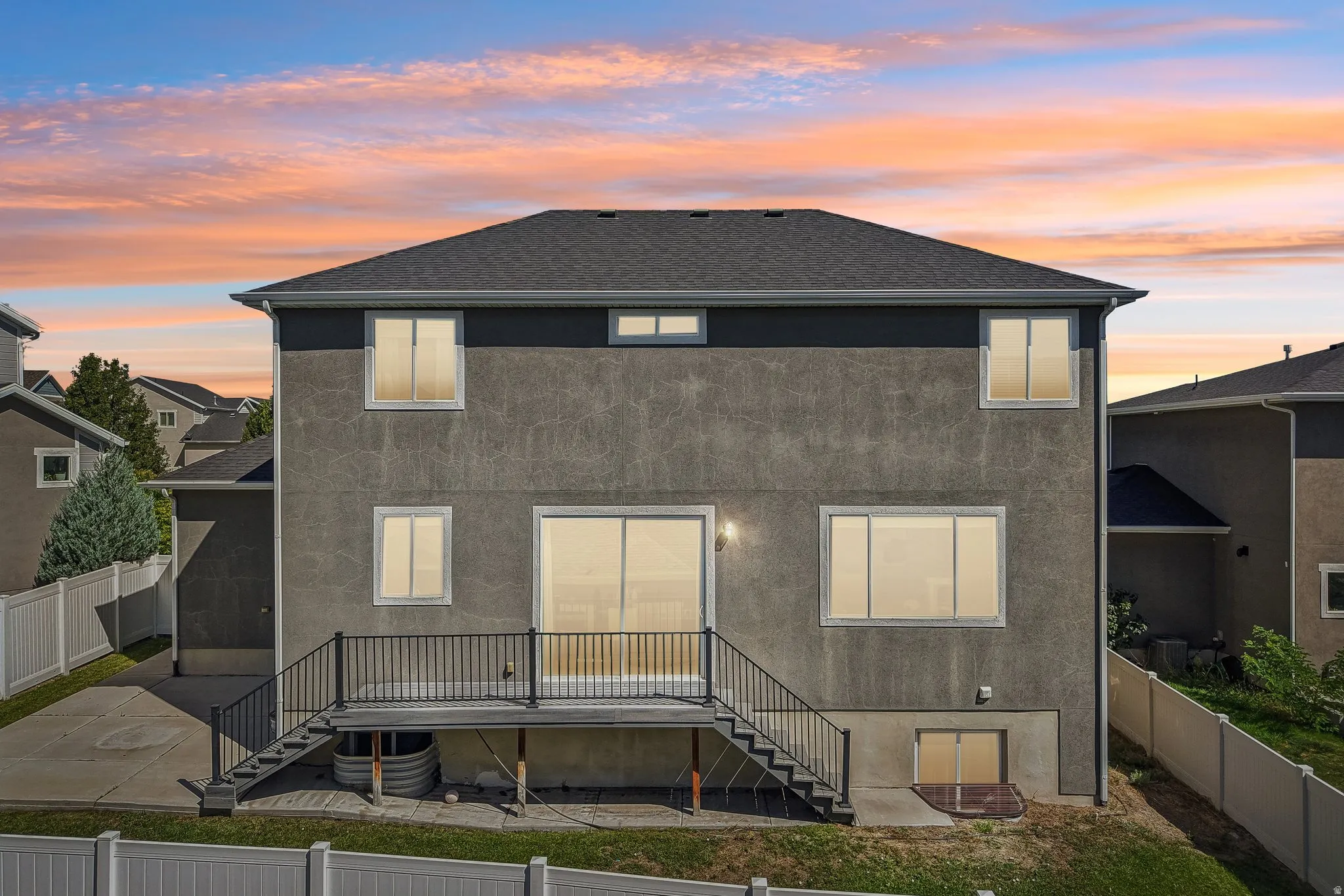 Stucco exterior with multiple windows, a sliding glass door, and a black metal deck railing