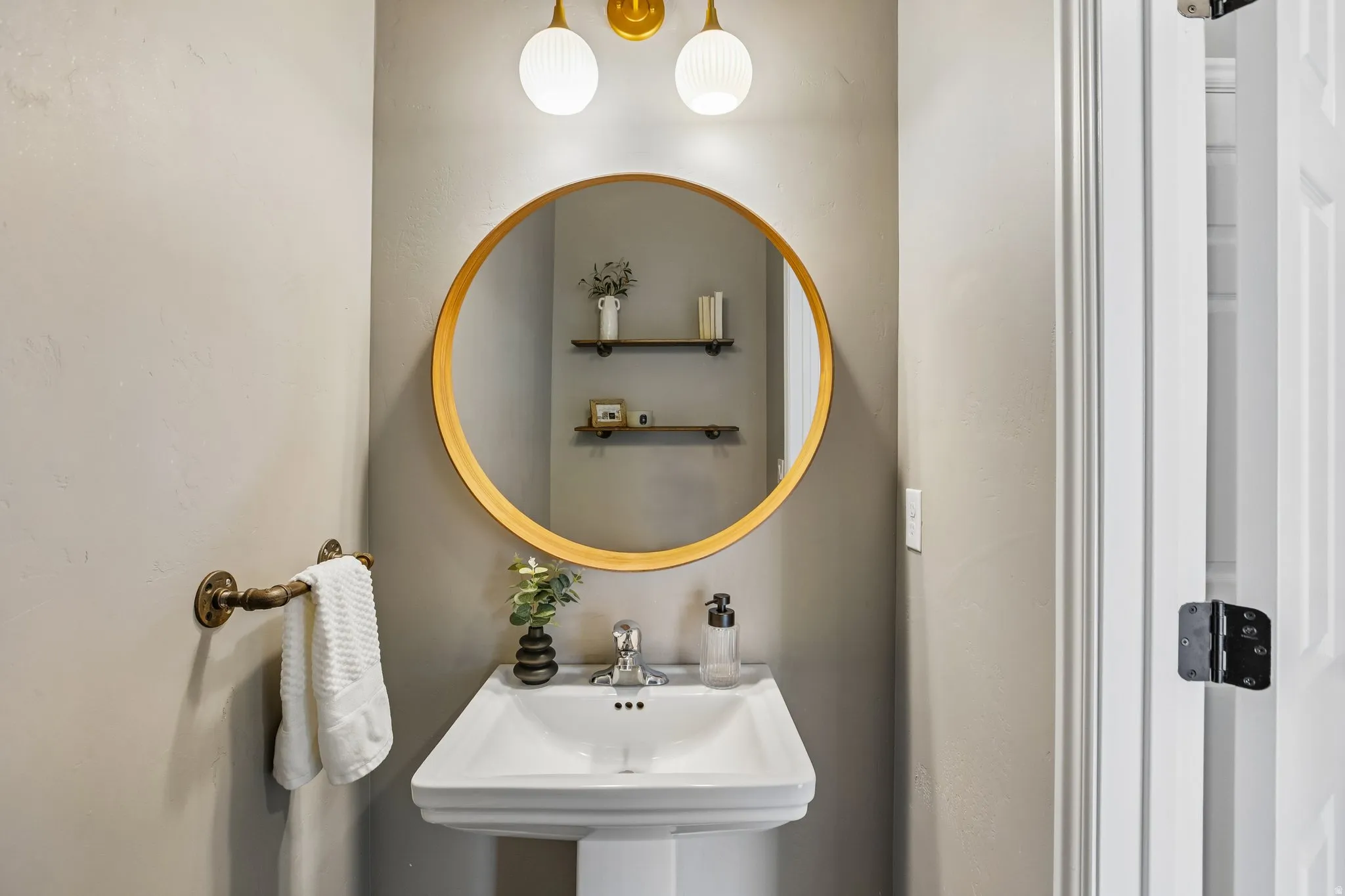 Pedestal sink with chrome-finish faucet, circular mirror, and wall-mounted lighting fixtures