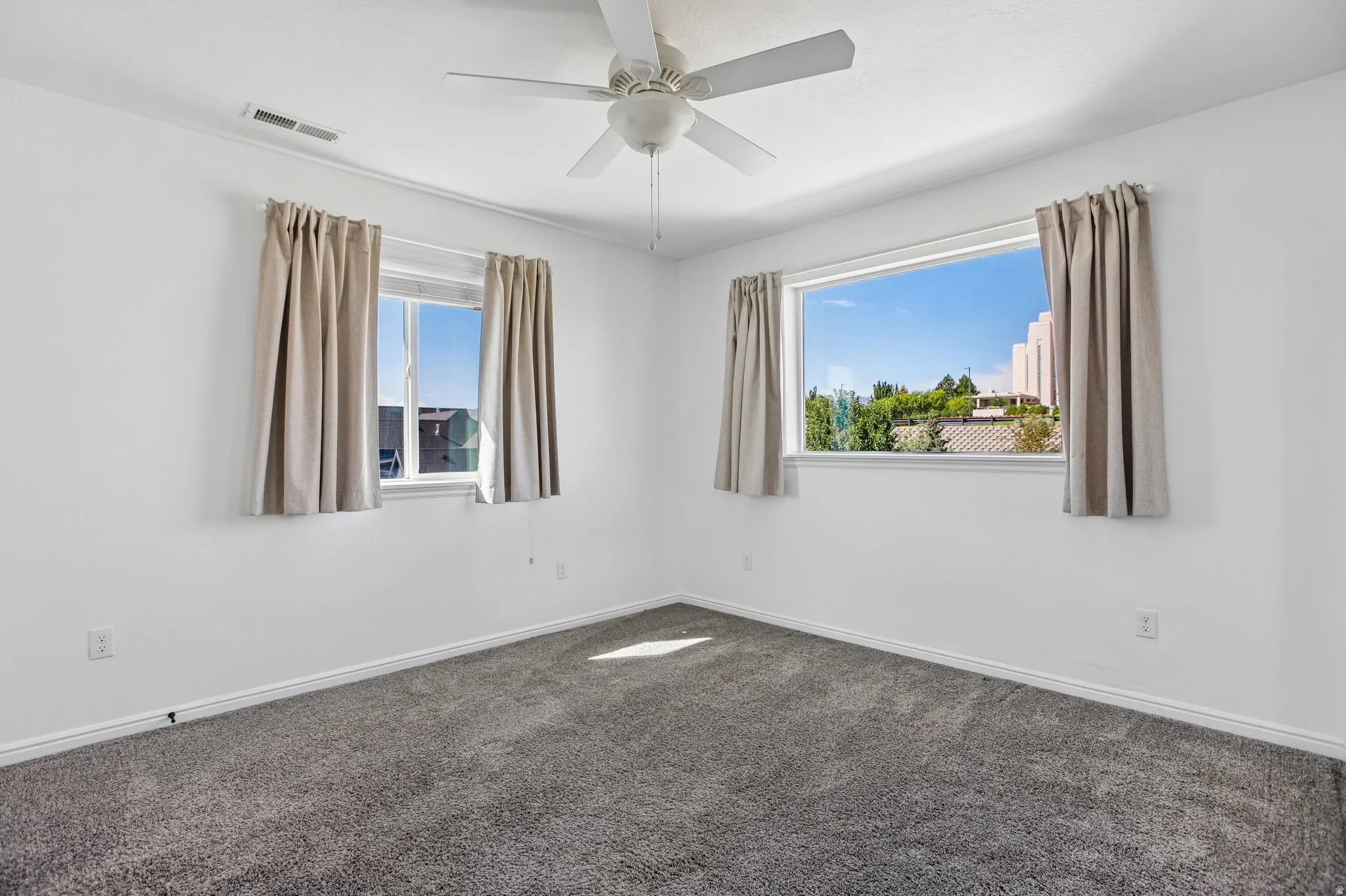 Spacious interior featuring neutral wall paint, gray carpeting, a ceiling fan, and multiple windows