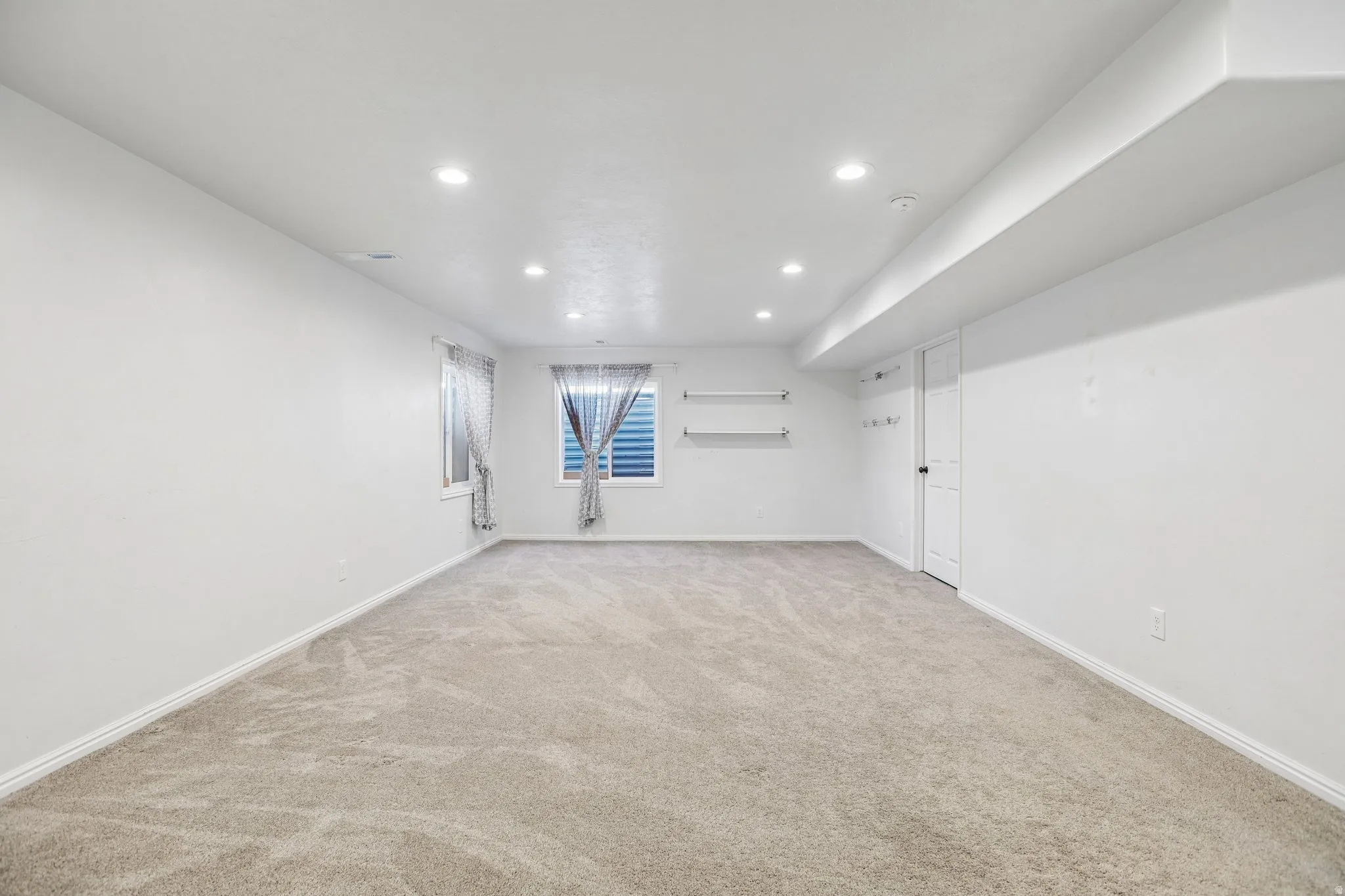 Recessed lighting, light-toned carpeting, two windows with horizontal blinds, built-in shelving, and a panel door