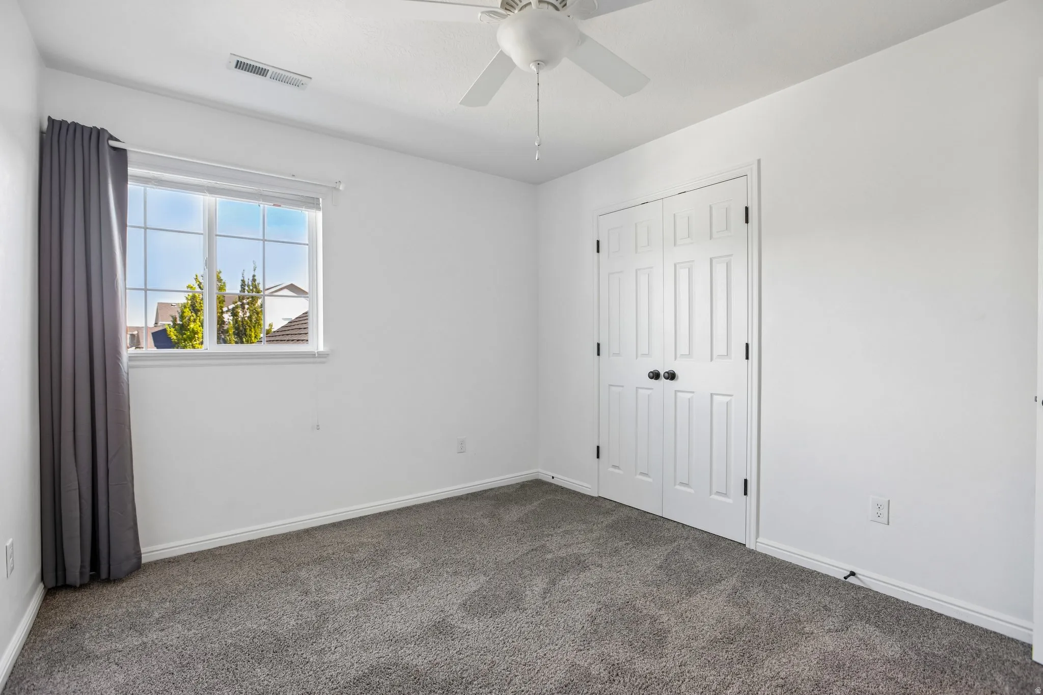 Neutral paint palette, grey carpet flooring, ceiling fan with light, white trim, and double closet doors with black hardware