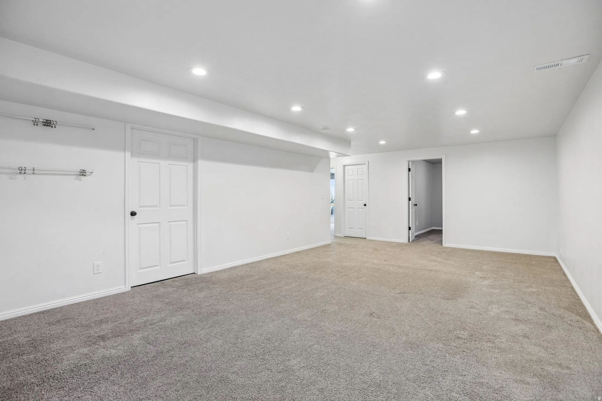 Recessed lighting illuminates the carpeted room, featuring white walls and white interior doors