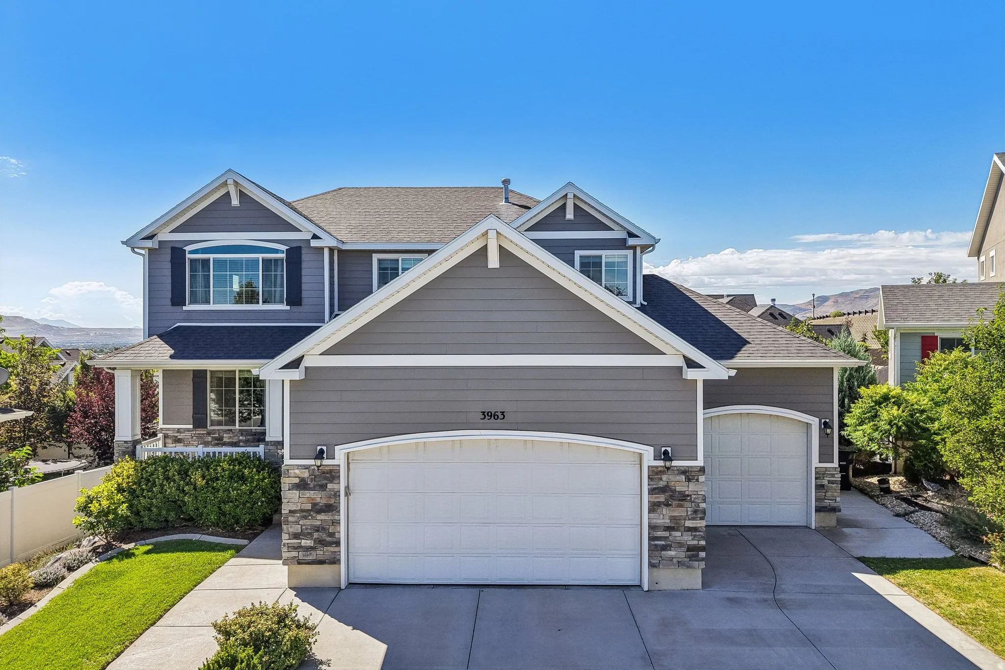 Two-story exterior with siding and stone accents, featuring a two-car garage, a single-car garage, and a covered front porch