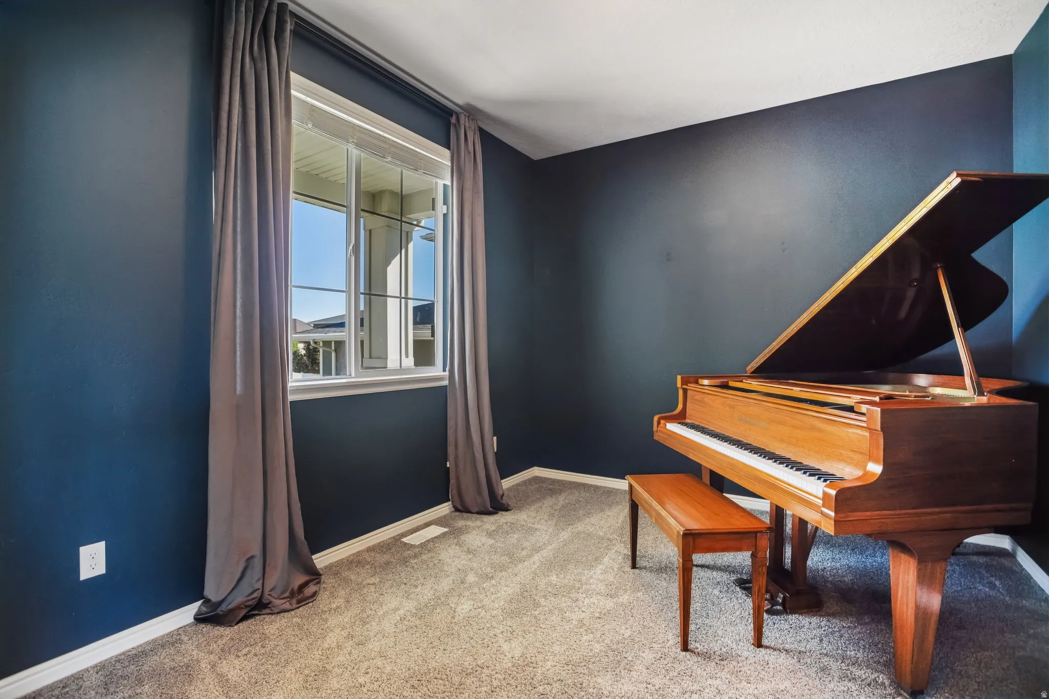 Dedicated music room featuring deep blue accent walls, large double-hung windows with gray drapery, neutral carpeting, and abundant natural light