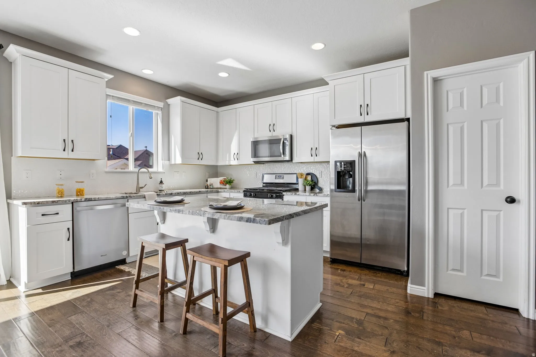 Kitchen featuring white cabinetry, stainless steel appliances, an island with countertop seating, wood-finish flooring, and recessed lighting