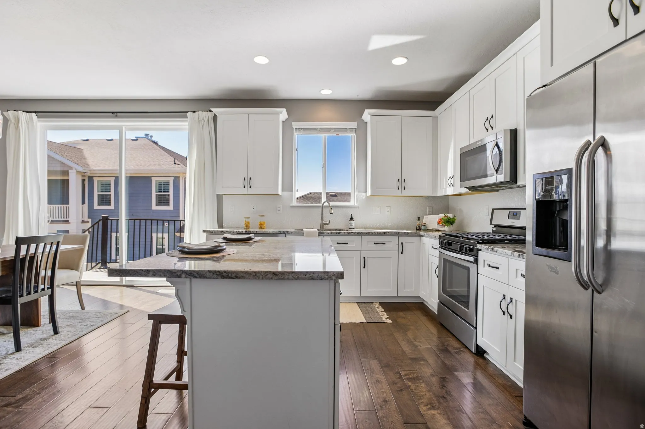 Kitchen featuring white cabinetry, stainless steel appliances, a large island with a stone countertop, wood-finish flooring, and a sliding glass door