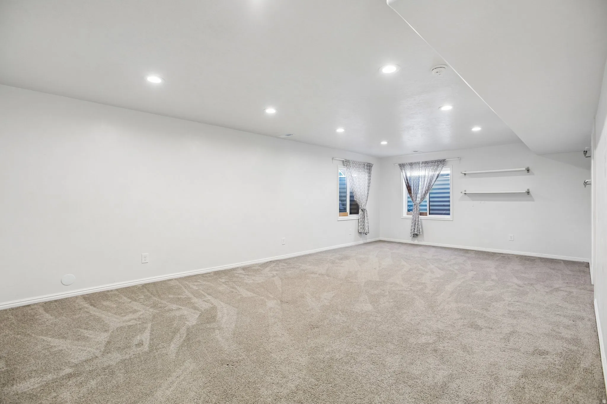 Recessed ceiling lighting, two windows, two wall-mounted shelves, and neutral carpet flooring