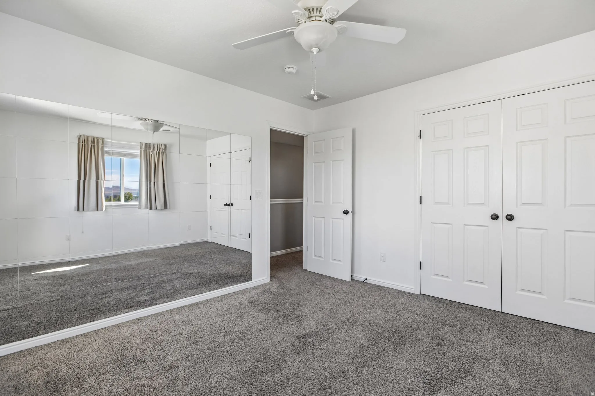 Plush carpet flooring, ceiling fan, mirrored accent wall, and two paneled closet doors