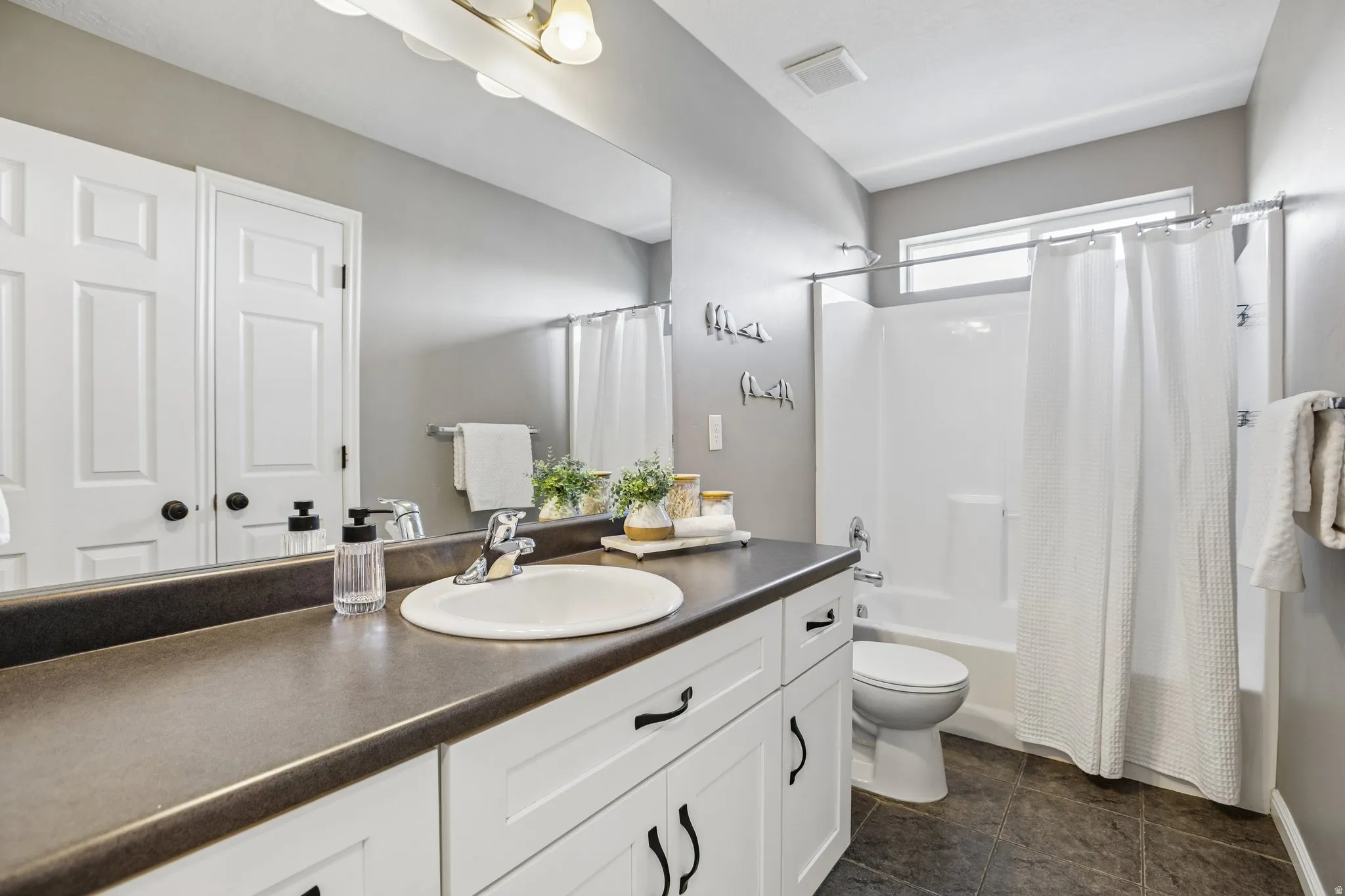 Full vanity mirror, white shaker-style cabinetry, dark countertop, single basin sink, and an integrated shower/tub unit