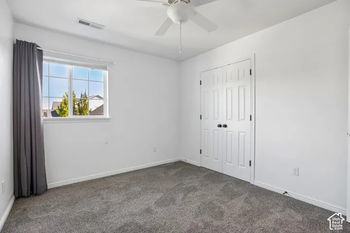 Neutral paint palette, grey carpet flooring, ceiling fan with light, white trim, and double closet doors with black hardware