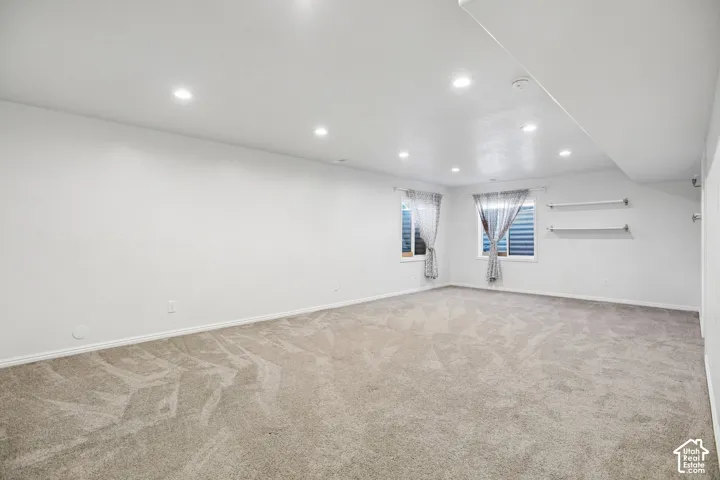 Recessed ceiling lighting, two windows, two wall-mounted shelves, and neutral carpet flooring