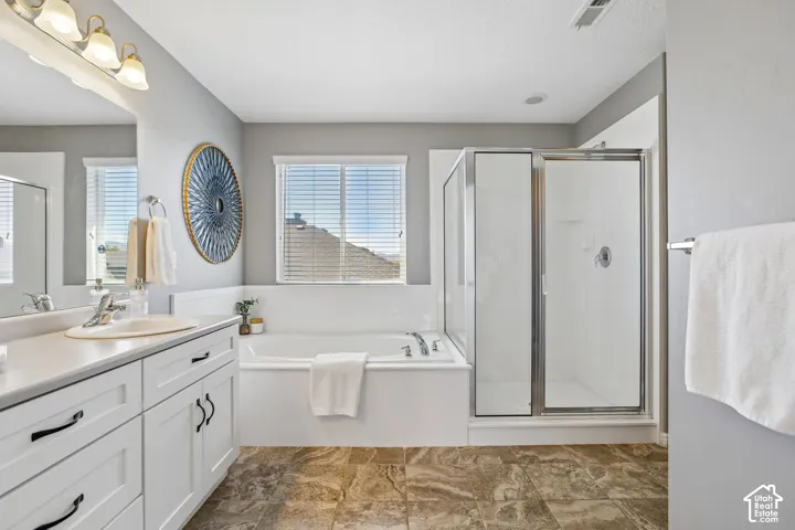 Bathroom featuring a built-in tub, separate shower with a glass enclosure, dual-sink vanity, and tiled flooring