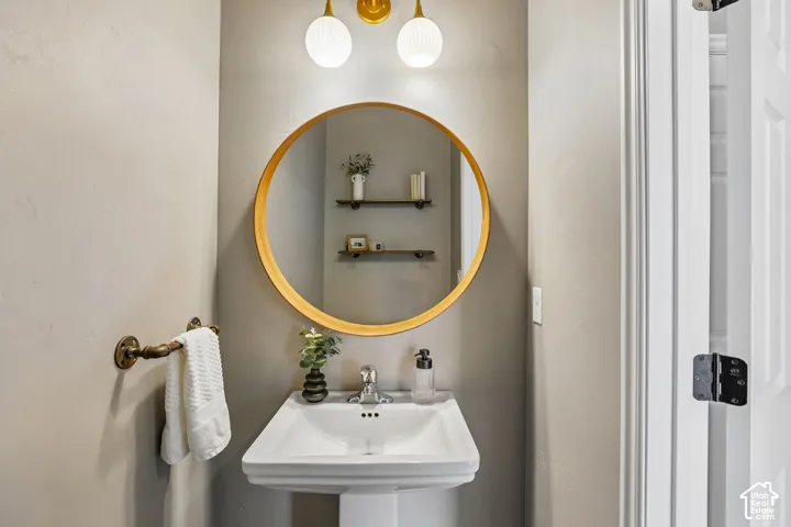 Pedestal sink with chrome-finish faucet, circular mirror, and wall-mounted lighting fixtures