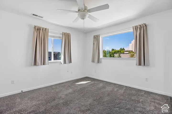 Spacious interior featuring neutral wall paint, gray carpeting, a ceiling fan, and multiple windows