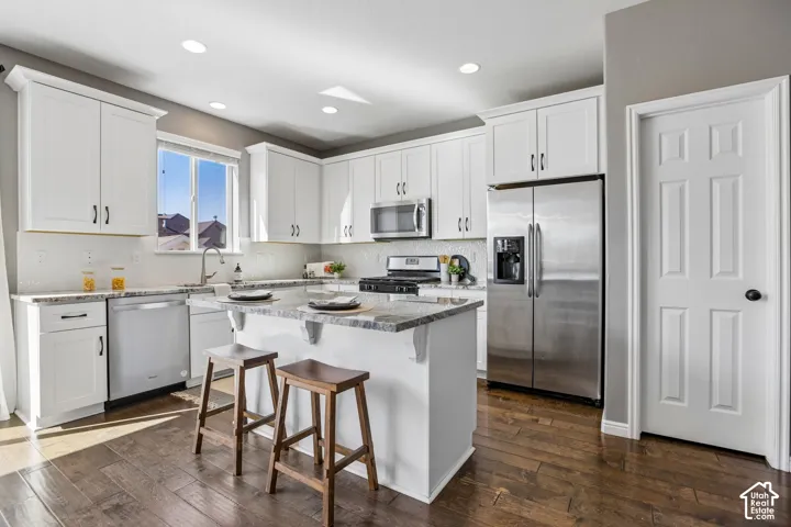 Kitchen featuring white cabinetry, stainless steel appliances, an island with countertop seating, wood-finish flooring, and recessed lighting