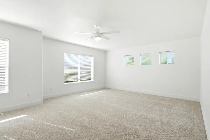 Spacious room featuring neutral carpet flooring, multiple windows, and a ceiling fan with integrated lighting