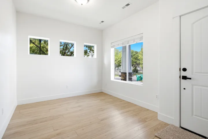 Wood-finish flooring, white paneled door with matte black hardware, recessed ceiling lighting, and multiple windows