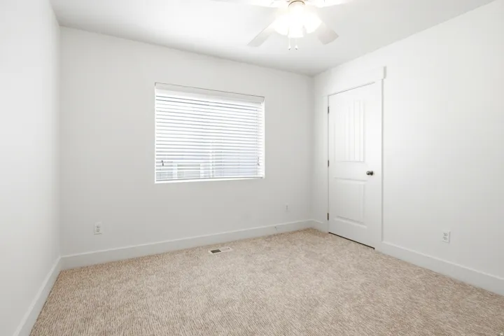 Neutral tone carpeting, white walls, and a ceiling fan with integrated lighting