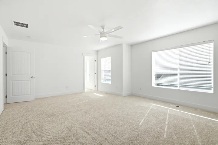 Expansive room featuring light-toned carpeting, white walls, and a ceiling fan with integrated lighting