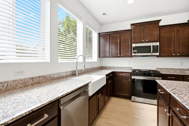 Kitchen featuring granite countertops, wood-finish flooring, dark wood cabinetry, a farmhouse sink with a gooseneck faucet, and stainless steel appliances