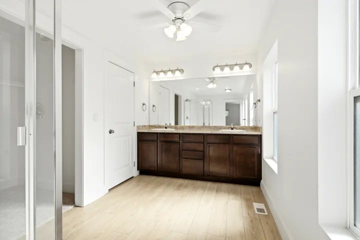 Dual vanity with an extended countertop, wood-finish cabinetry, and light wood-finish flooring