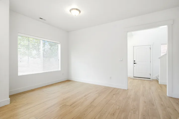 Wood-finish flooring, white walls, and a window with horizontal blinds provide a bright interior