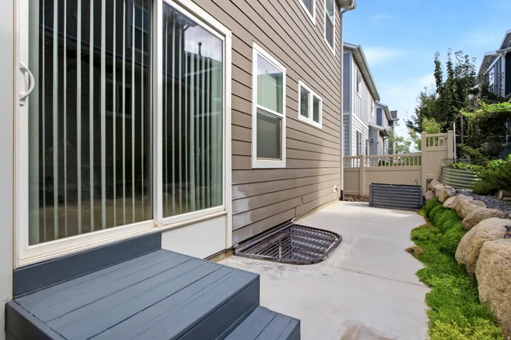 Sliding glass door, exterior steps, window well, rock landscaping, and concrete pathway