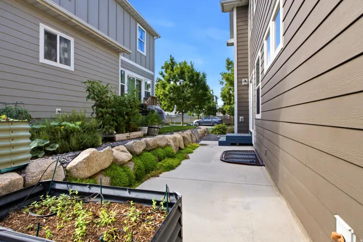 Side yard featuring concrete pathway, rock retaining wall, established plantings, and horizontal siding