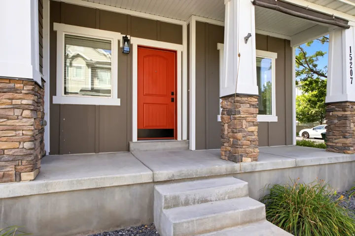 Welcoming front porch featuring a vibrant orange entry door, stone-clad columns, and concrete steps