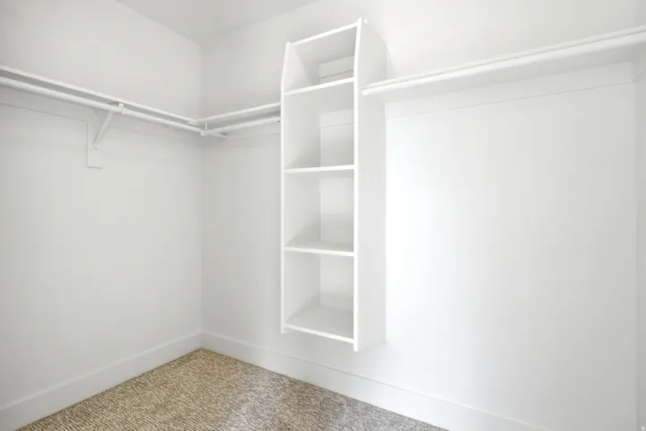 Built-in shelving unit, dual hanging rods, light-colored carpeting, white baseboards, and white walls