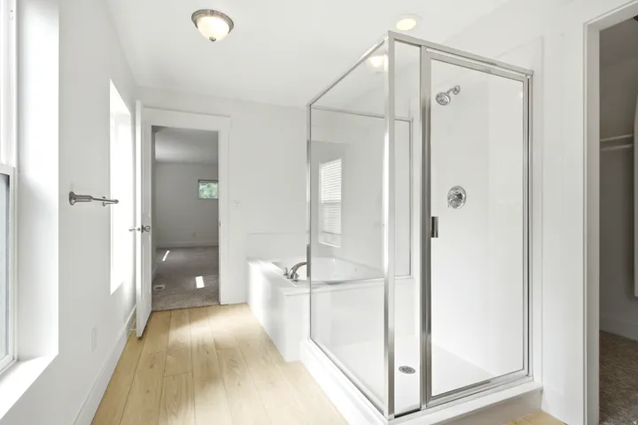 Wood-finish flooring, glass-enclosed shower, built-in bathtub, and recessed lighting