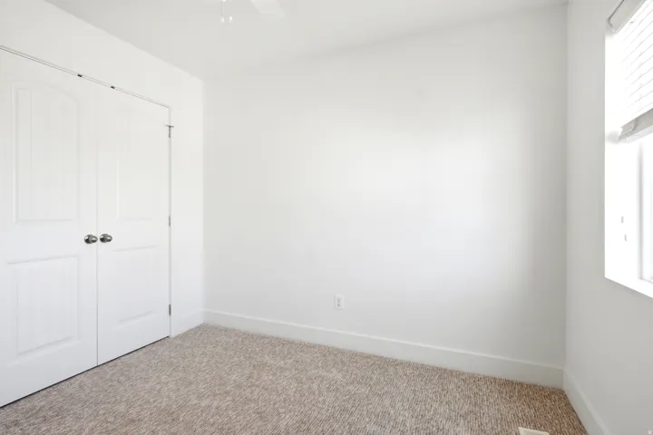 Neutral wall paint, textured carpet, window with blinds, ceiling fan, and bi-fold closet doors
