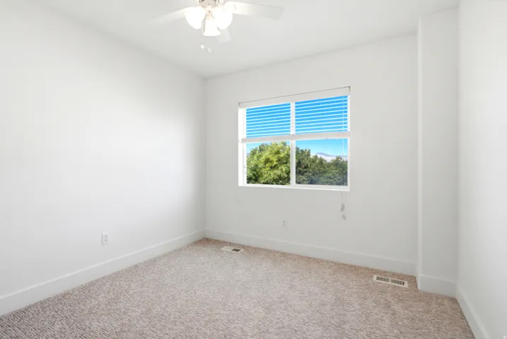 Neutral color palette with textured carpeting, a window featuring horizontal blinds, and a ceiling fan