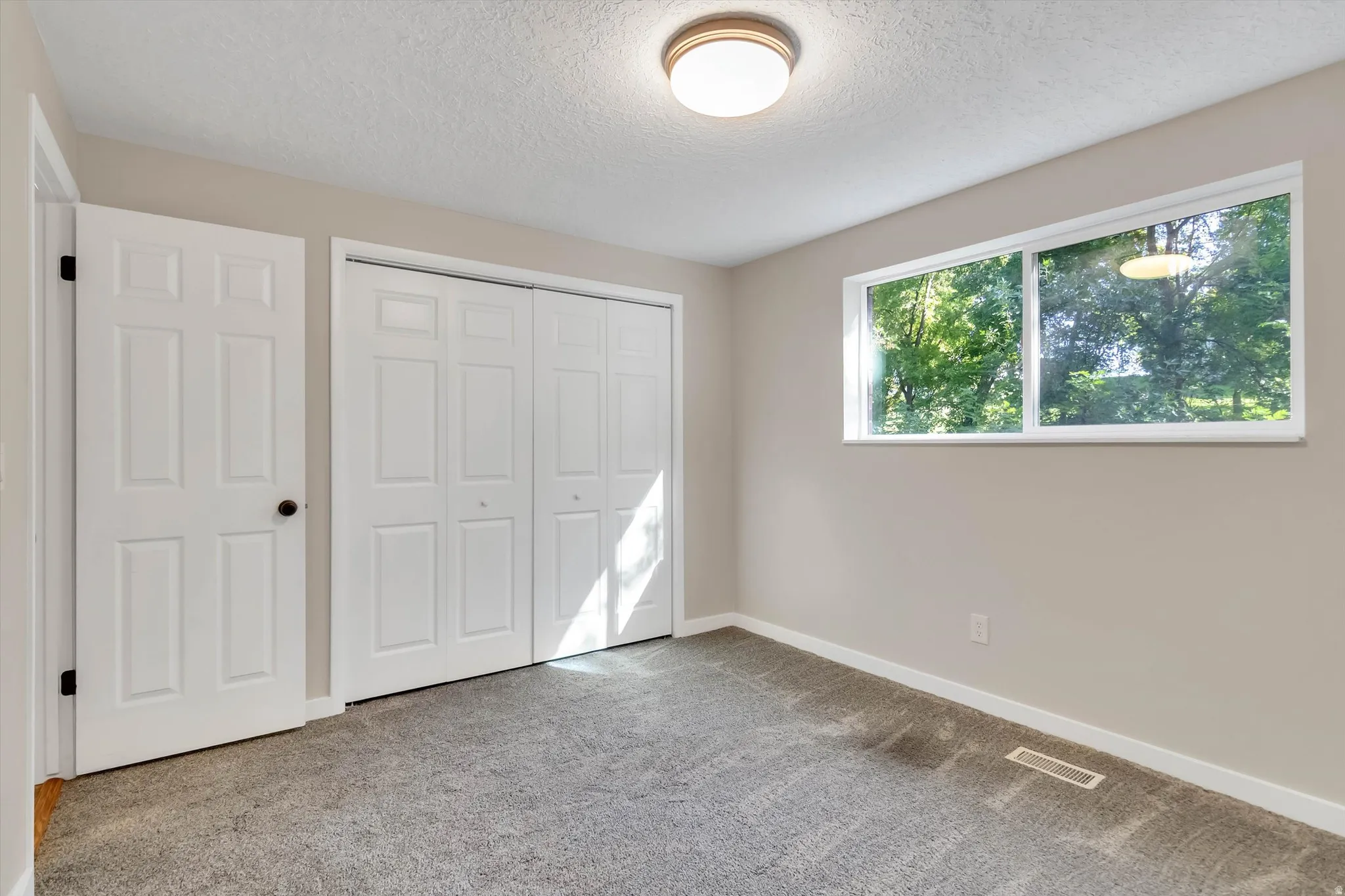 Light gray wall paint, textured ceiling, gray carpet, white trim, and a horizontal window