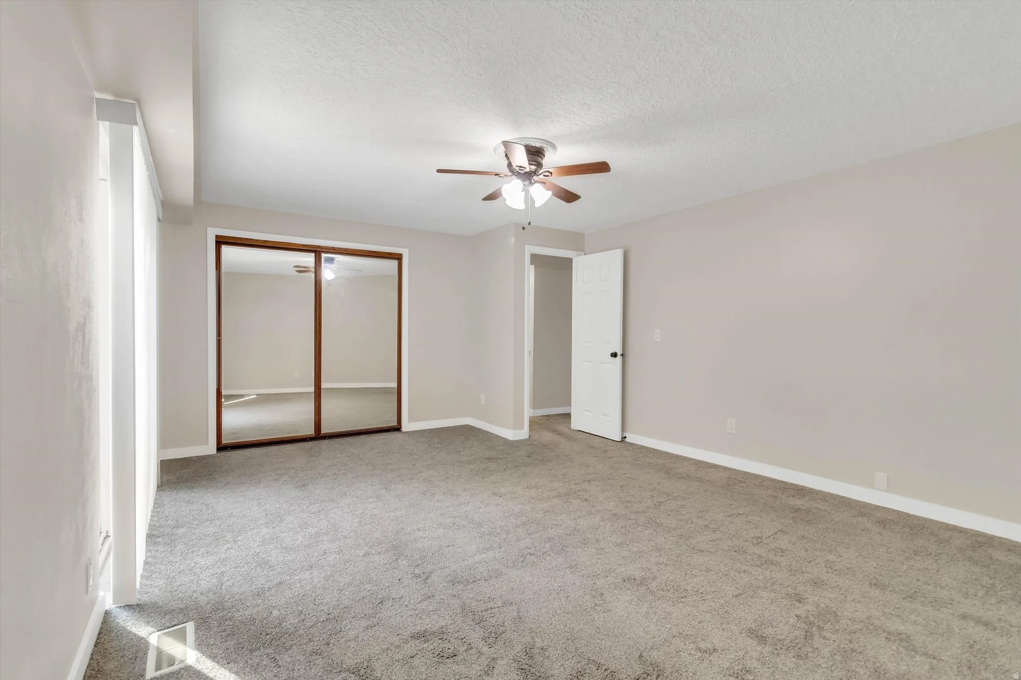 Wall-to-wall carpeting with light neutral walls, a ceiling fan with integrated lighting, and a mirrored closet