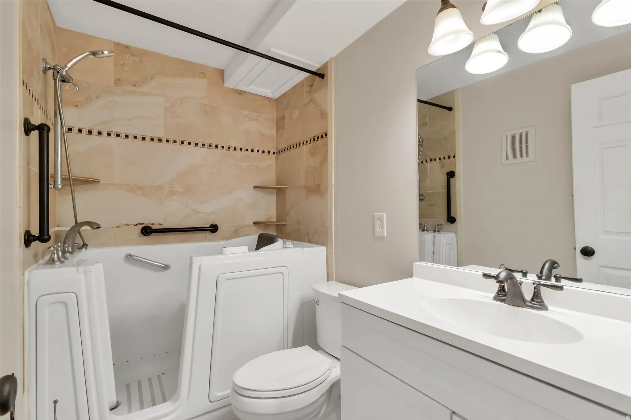 Walk-in tub with grab bars, tiled shower surround, integrated shelving, vanity with single sink, and wall-mounted mirror