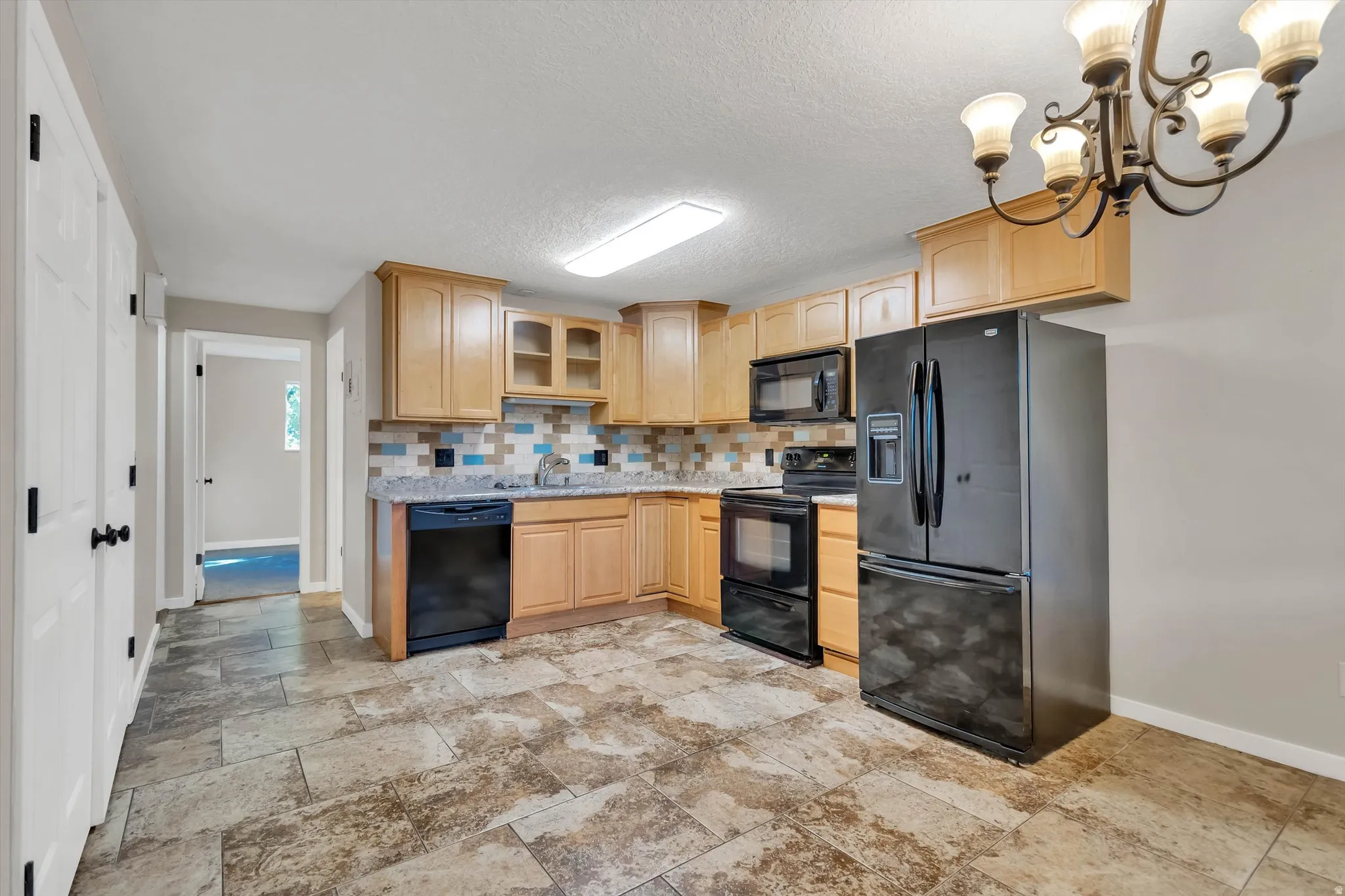 Functional kitchen featuring wood-finish cabinetry, black appliances, stone-look flooring, and a tiled backsplash