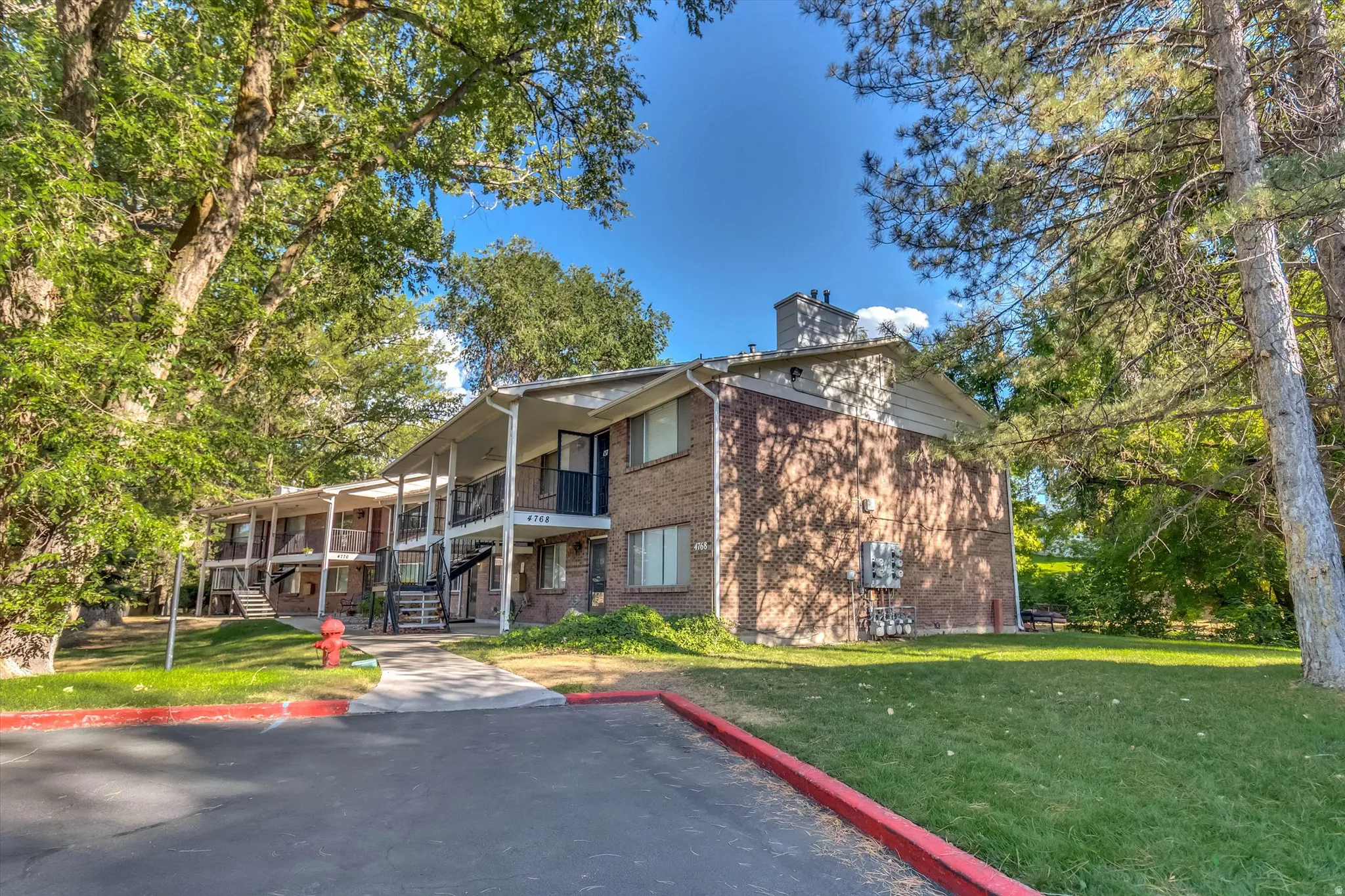 Brick exterior building with multiple balconies, surrounded by mature trees and green lawn