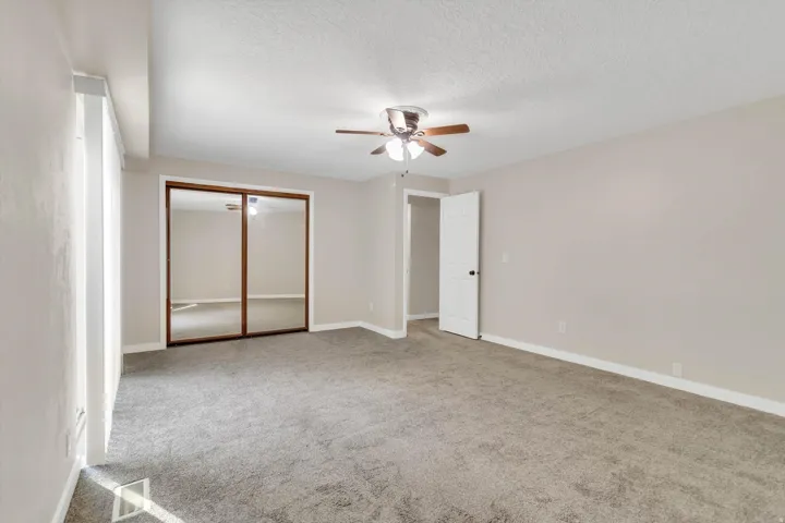 Wall-to-wall carpeting with light neutral walls, a ceiling fan with integrated lighting, and a mirrored closet